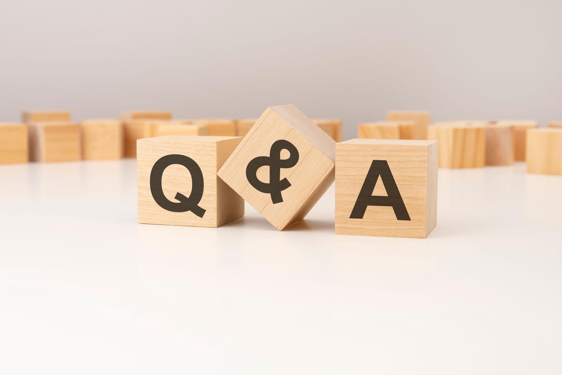 three wooden cubes with Q and A symbols on them. white background. in the background there are many wooden blocks of different sizes